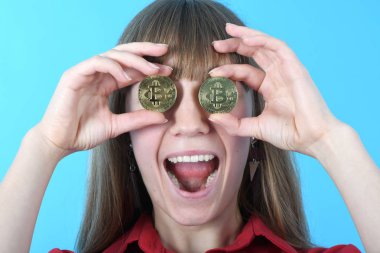 Güzel kadın göz yerine iki altın cryptocurrency bitcoin mavi arka plan üzerinde elinde tutar