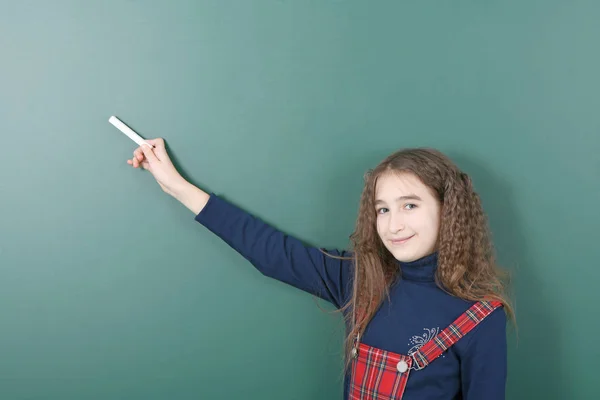 Školka u zelené školní tabule. Mladá hravý dívka drží křídu v ruce. — Stock fotografie