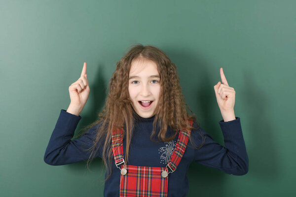 Schoolgirl near green school board. Young playful girl shows a finger up.