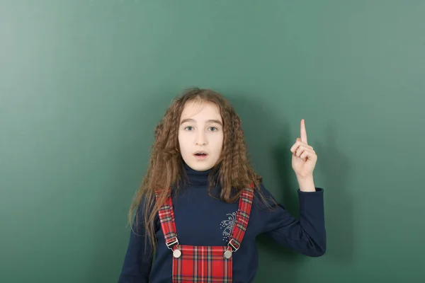 Studentessa vicino al consiglio scolastico verde. Giovane ragazza giocosa mostra un dito in su . — Foto Stock