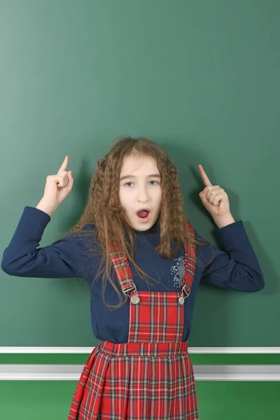 Schoolgirl near green school board. Young playful girl shows a finger up. — Stock Photo, Image