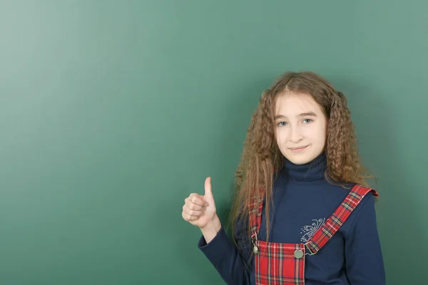 Estudante perto do conselho escolar verde. Jovem menina brincalhão mostra um dedo para cima . — Fotografia de Stock
