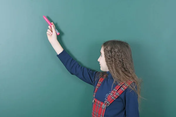 Schoolgirl near green school board. Young playful girl holds a red pen in her hand. Royalty Free Stock Images