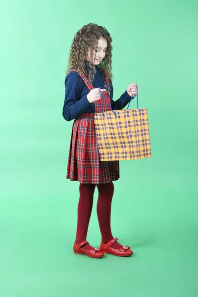 Niño con una textura a cuadros de embalaje amarillo aislado sobre fondo verde. Regalo de vacaciones, compras . — Foto de Stock