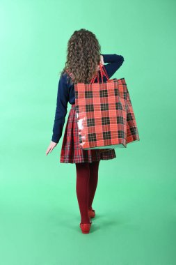Yeşil arka planda yalıtılmış kırmızı bir paket olan çocuk. Küçük güzellik alışverişkolik. Tatil hediyesi, alışveriş. 