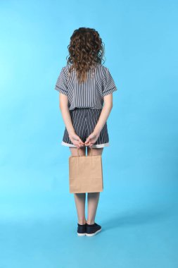 Mavi arka planda izole edilmiş bir paketolan çocuk. Tatil hediyesi, alışveriş. Alışveriş merkezinde çocuk mutlu alışveriş. 