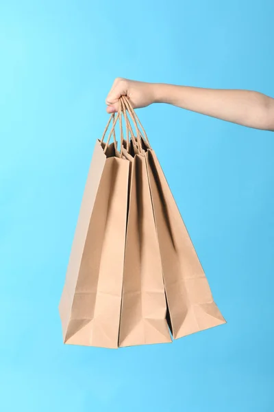 Criança mão segurando sacos de compras de papel isolado no fundo azul . — Fotografia de Stock