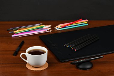 Profesyonel grafik tableti, kahve fincanı, dijitalleştirilmiş ve ahşap masa üzerinde çok renkli kalemler. Yüksek çözünürlüklü. Tam alan derinliği. Çalışma için tablo konsepti.