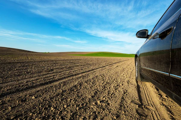 car on dirt road along green field on sunny day