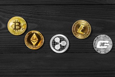 Ahşap zemin üzerinde bitcoin, dalgalanma ve ethereum sembollü gümüş ve altın sikkeler.