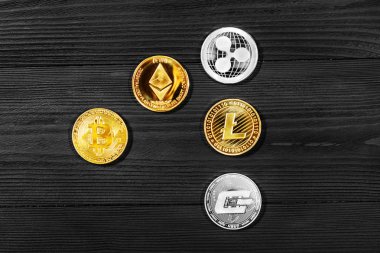 Ahşap zemin üzerinde bitcoin, dalgalanma ve ethereum sembollü gümüş ve altın sikkeler.