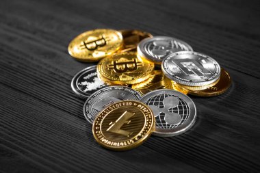 Ahşap zemin üzerinde bitcoin, dalgalanma ve ethereum sembollü gümüş ve altın sikkeler.