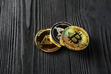 Ahşap zemin üzerinde bitcoin, dalgalanma ve ethereum sembollü gümüş ve altın sikkeler.