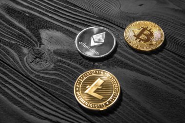 Ahşap zemin üzerinde bitcoin, dalgalanma ve ethereum sembollü gümüş ve altın sikkeler.