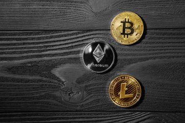 Ahşap zemin üzerinde bitcoin, dalgalanma ve ethereum sembollü gümüş ve altın sikkeler.