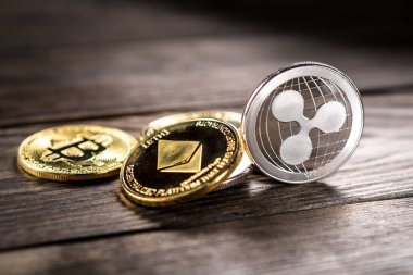 Ahşap zemin üzerinde bitcoin, dalgalanma ve ethereum sembollü gümüş ve altın sikkeler.