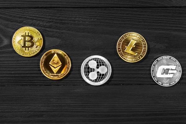 Ahşap zemin üzerinde bitcoin, dalgalanma ve ethereum sembollü gümüş ve altın sikkeler.