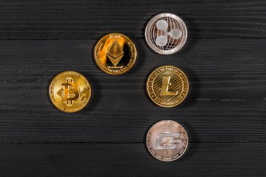 Ahşap zemin üzerinde bitcoin, dalgalanma ve ethereum sembollü gümüş ve altın sikkeler.