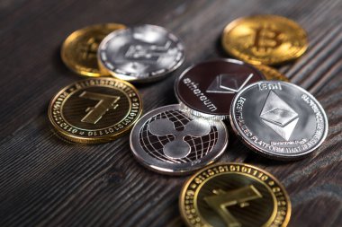 Ahşap zemin üzerinde bitcoin, dalgalanma ve ethereum sembollü gümüş ve altın sikkeler.