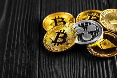 Ahşap zemin üzerinde bitcoin, dalgalanma ve ethereum sembollü gümüş ve altın sikkeler.
