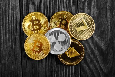 Ahşap zemin üzerinde bitcoin, dalgalanma ve ethereum sembollü gümüş ve altın sikkeler.