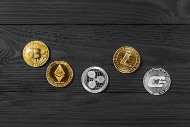 Ahşap zemin üzerinde bitcoin, dalgalanma ve ethereum sembollü gümüş ve altın sikkeler.