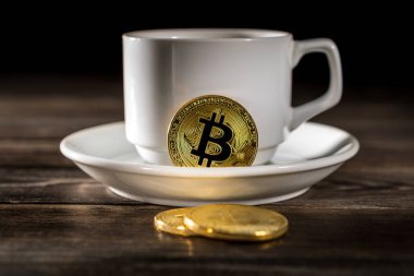 Tahta bir arka planda izole edilmiş kahve fincanının üzerinde duran kripto altın bitcoin.