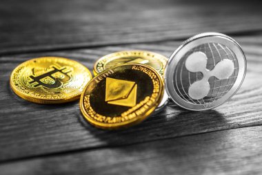 Ahşap zemin üzerinde bitcoin, dalgalanma ve ethereum sembollü gümüş ve altın sikkeler.