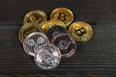 Ahşap zemin üzerinde bitcoin, dalgalanma ve ethereum sembollü gümüş ve altın sikkeler.