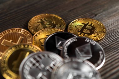 Ahşap zemin üzerinde bitcoin, dalgalanma ve ethereum sembollü gümüş ve altın sikkeler.