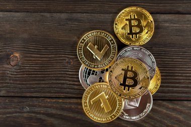 Ahşap zemin üzerinde bitcoin, dalgalanma ve ethereum sembollü gümüş ve altın sikkeler.