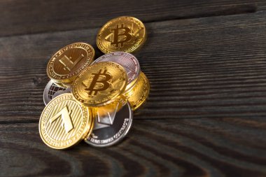 Ahşap zemin üzerinde bitcoin, dalgalanma ve ethereum sembollü gümüş ve altın sikkeler.