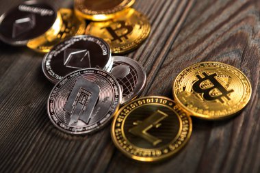 Ahşap zemin üzerinde bitcoin, dalgalanma ve ethereum sembollü gümüş ve altın sikkeler.