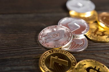 Ahşap zemin üzerinde bitcoin, dalgalanma ve ethereum sembollü gümüş ve altın sikkeler.