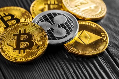 Ahşap zemin üzerinde bitcoin, dalgalanma ve ethereum sembollü gümüş ve altın sikkeler.