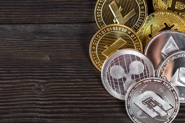 Ahşap zemin üzerinde bitcoin, dalgalanma ve ethereum sembollü gümüş ve altın sikkeler.