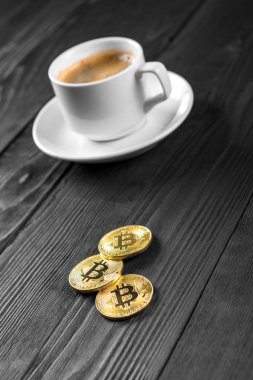 Tahta bir arka planda izole edilmiş kahve fincanının üzerinde duran kripto altın bitcoin.