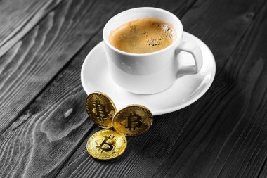 Tahta bir arka planda izole edilmiş kahve fincanının üzerinde duran kripto altın bitcoin.