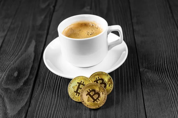 Tahta bir arka planda izole edilmiş kahve fincanının üzerinde duran kripto altın bitcoin.