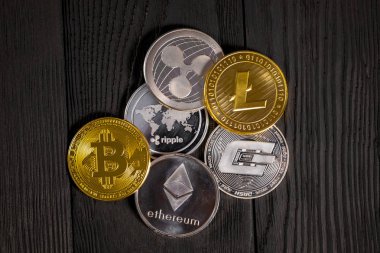 Ahşap zemin üzerinde bitcoin, dalgalanma ve ethereum sembollü gümüş ve altın sikkeler.