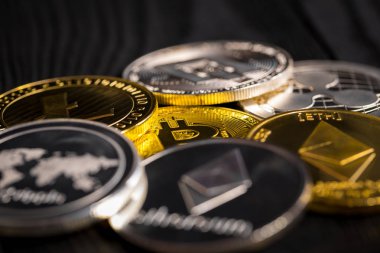 Ahşap zemin üzerinde bitcoin, dalgalanma ve ethereum sembollü gümüş ve altın sikkeler.
