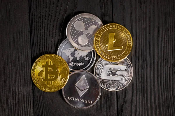 Ahşap zemin üzerinde bitcoin, dalgalanma ve ethereum sembollü gümüş ve altın sikkeler.