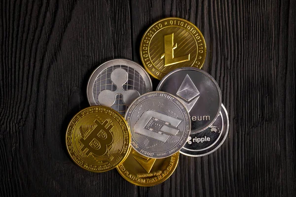 Ahşap zemin üzerinde bitcoin, dalgalanma ve ethereum sembollü gümüş ve altın sikkeler.