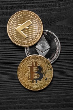 Ahşap zemin üzerinde bitcoin, dalgalanma ve ethereum sembollü gümüş ve altın sikkeler.