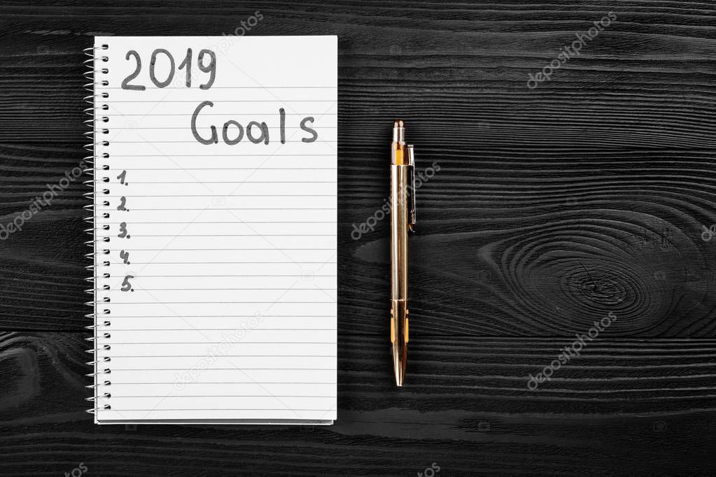 2019 GOALS on his notebook. New year resolutions concept. Top view.