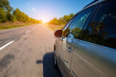 Genç adam asfalt yolda modern arabayı kullanıyor.