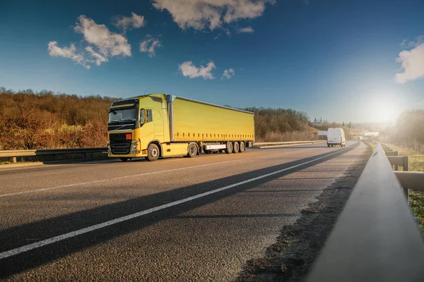 Aankomst witte vrachtwagen op de weg in een landelijk landschap bij zonsondergang — Stockfoto