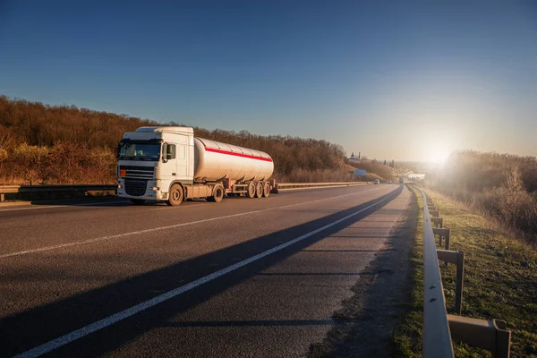 Aankomst witte vrachtwagen op de weg in een landelijk landschap bij zonsondergang — Stockfoto