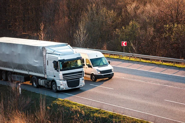 Aankomst witte vrachtwagen op de weg in een landelijk landschap bij zonsondergang — Stockfoto