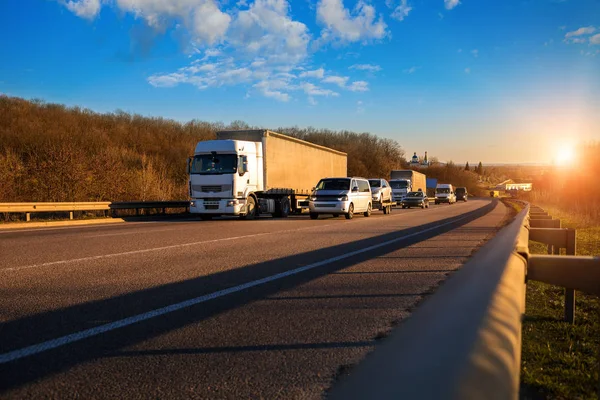 Aankomst witte vrachtwagen op de weg in een landelijk landschap bij zonsondergang — Stockfoto